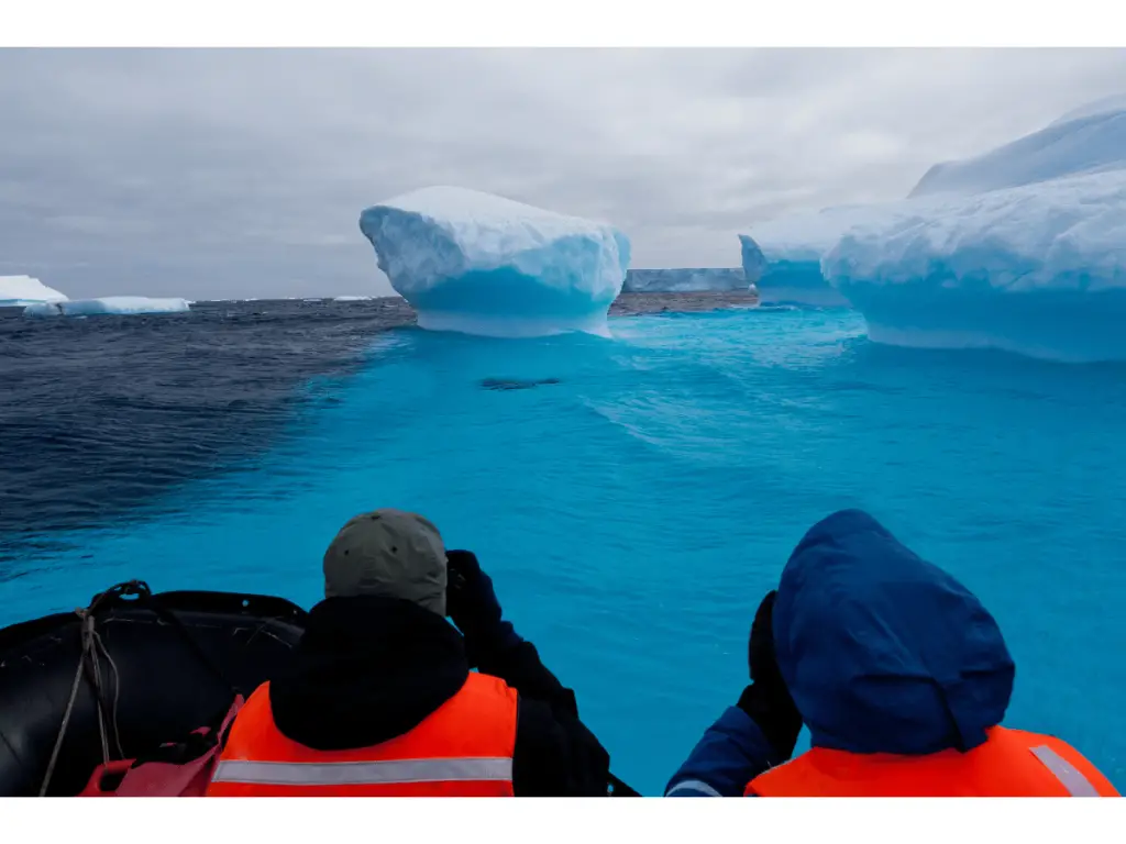 Two tourists on a zodiac vessel inspecting icebergs in Antarctica waters