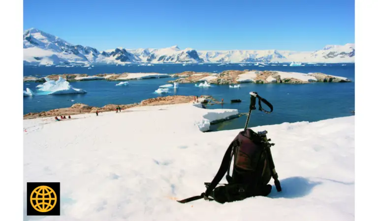 A black backpack on the snow with a view of glaciers and sea